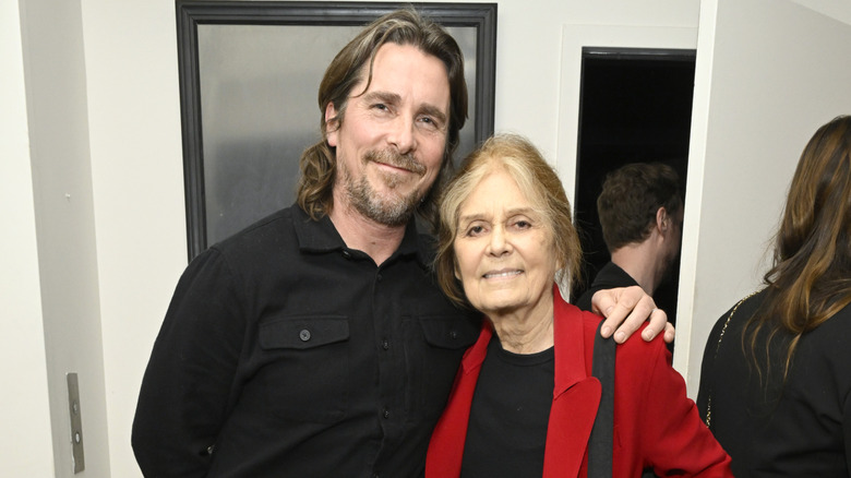 Christian Bale smiling with his arm around Gloria Steinem