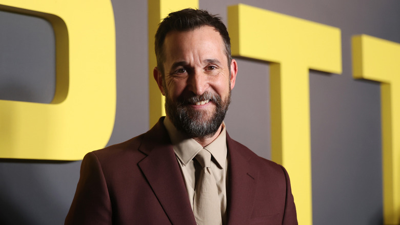 Noah Wyle posing in maroon colored suit