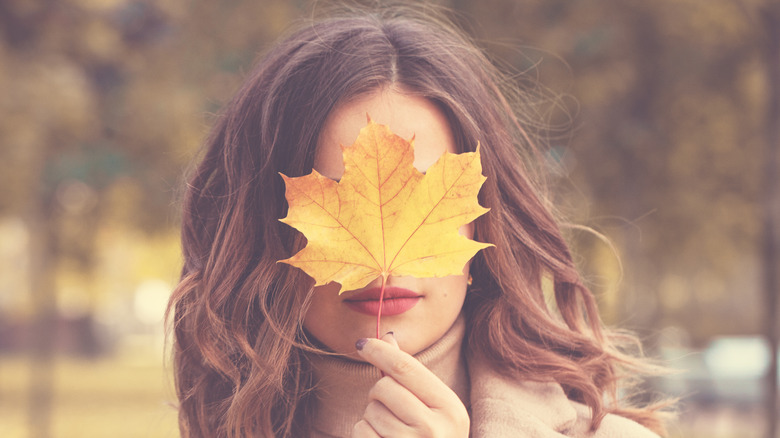 Woman holding fall time leaf over face