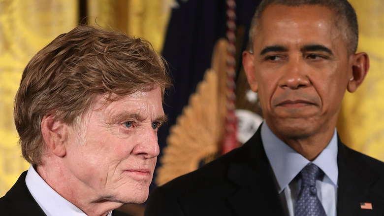 Barack Obama looking at Robert Redford as he stands behind him