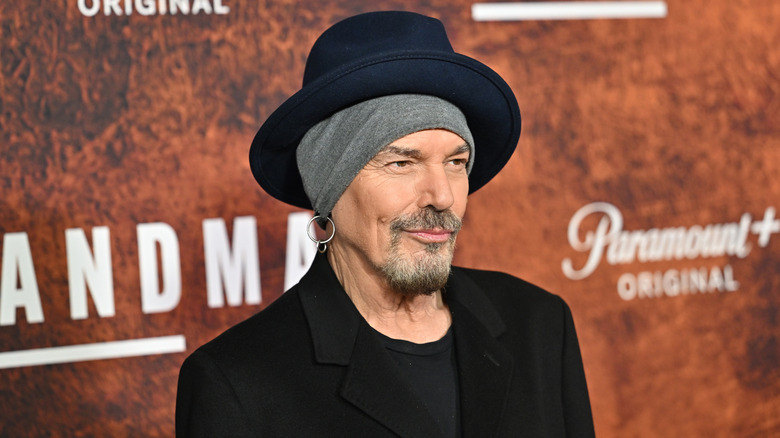 Billy Bob Thornton smirking while posing at an event in an all black outfit