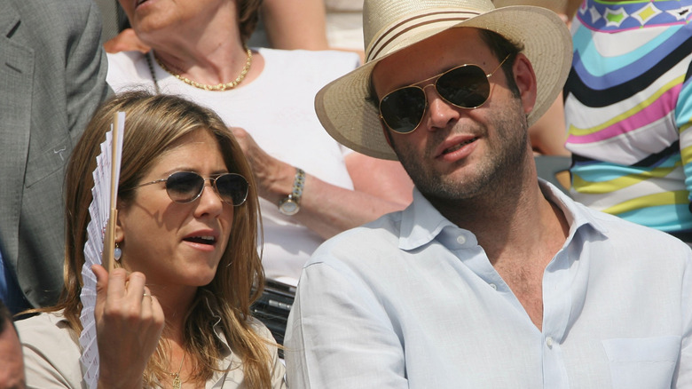 Jennifer Aniston and Vince Vaughn wearing sunglasses and sitting together in a crowd.