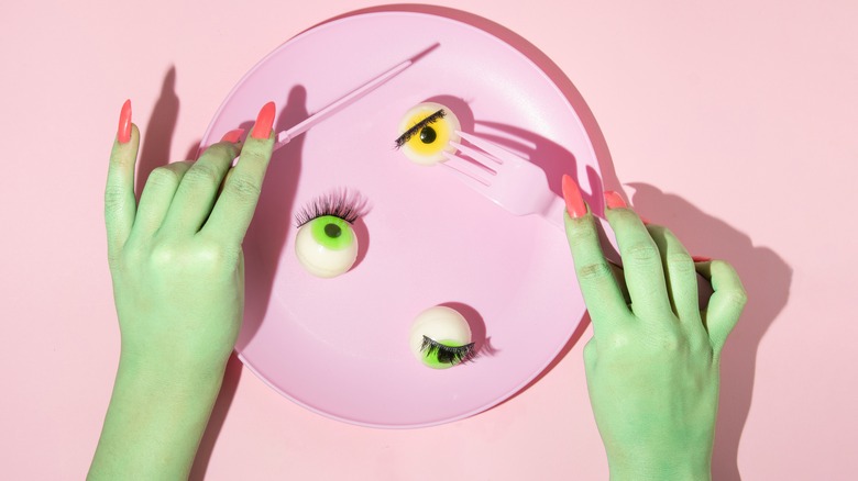 Surreal art with mannequin hands holding pink fork and knife and a plate with fake eyeballs