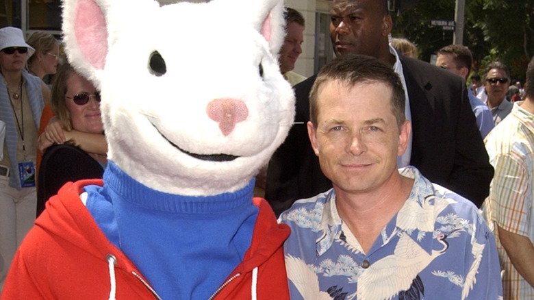 A person in a Stuart Little mascot costume posing for photos with a smiling Michael J. Fox