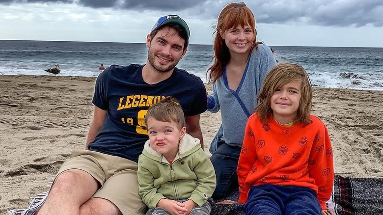 Actor Galadriel Steinman smiles sitting on the beach next to her husband and two sons in front of a cloudy sky
