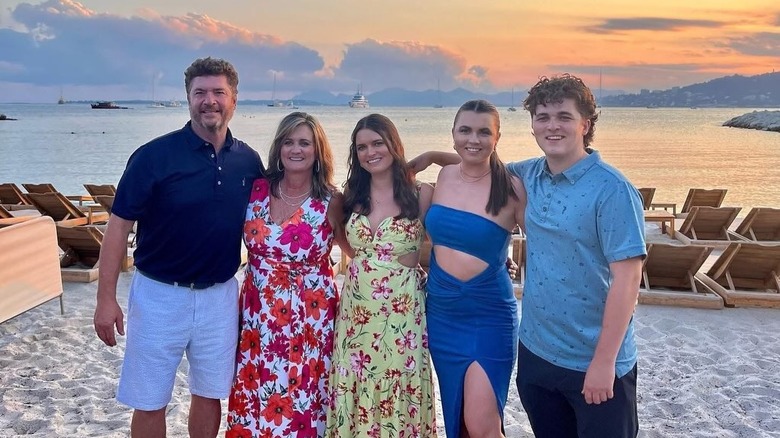 Pat Finn poses on the beach at sunset next to his wife and three kids who have their arms around each other smiling