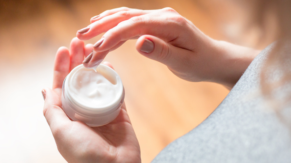 Woman dipping finger into jar of moisturizer