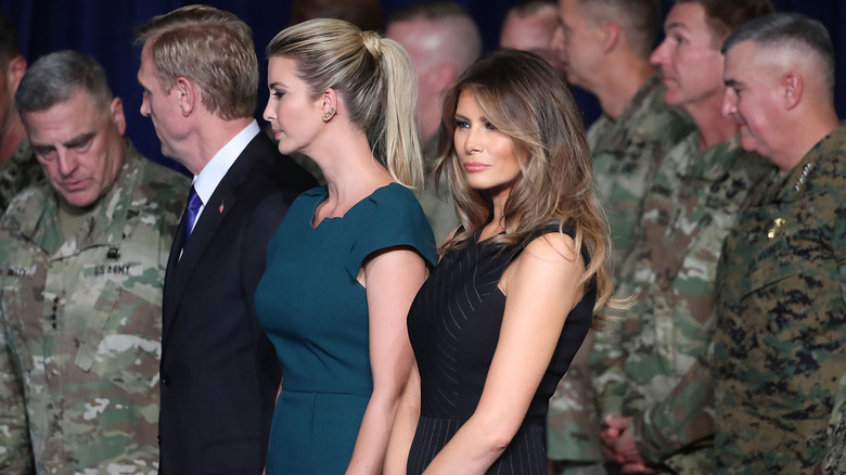Melania Trump and Ivanka Trump standing among military men in uniform.