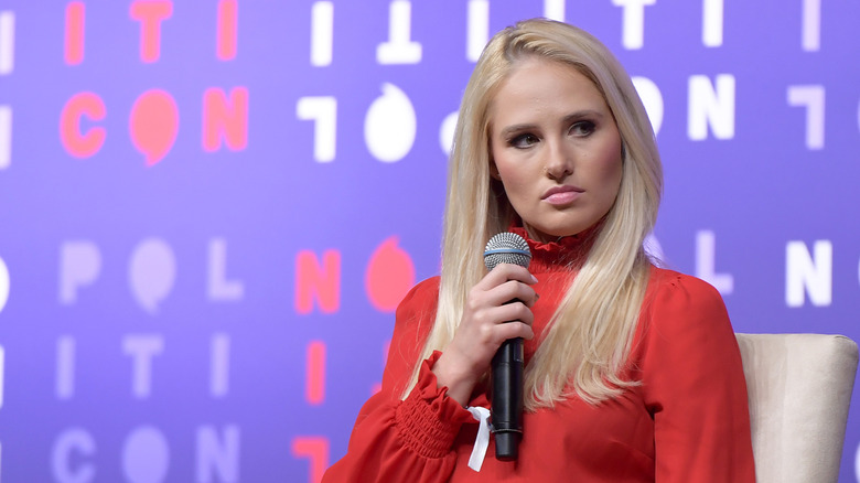 Tomi Lahren looking grumpy with a microphone in an all-red outfit