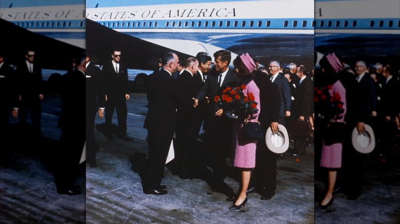 President John F. Kennedy and wife, Jackie Kennedy, are standing for group pictures next to a plane