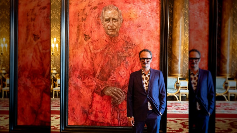 Artist Jonathan Yeo poses next to a blazing red portrait of King Charles III