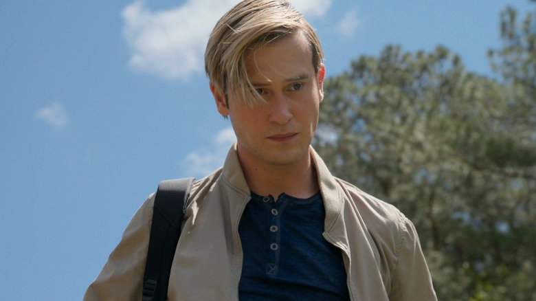 Tyler Henry standing outside in front of a tree and looking at the ground with a blue sky in the background