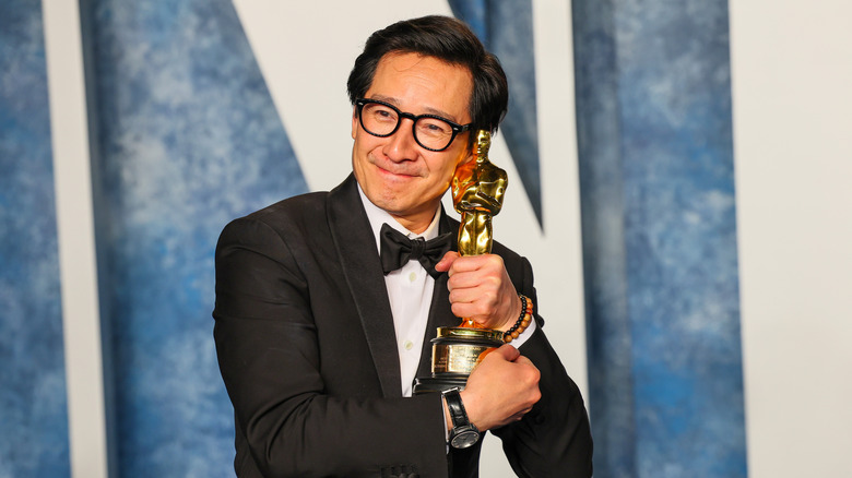 Ke Huy Quan smiling and holding his Oscar close to his face.