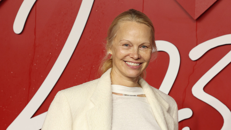 Pamela Anderson smiling without makeup in a white top and jacket.