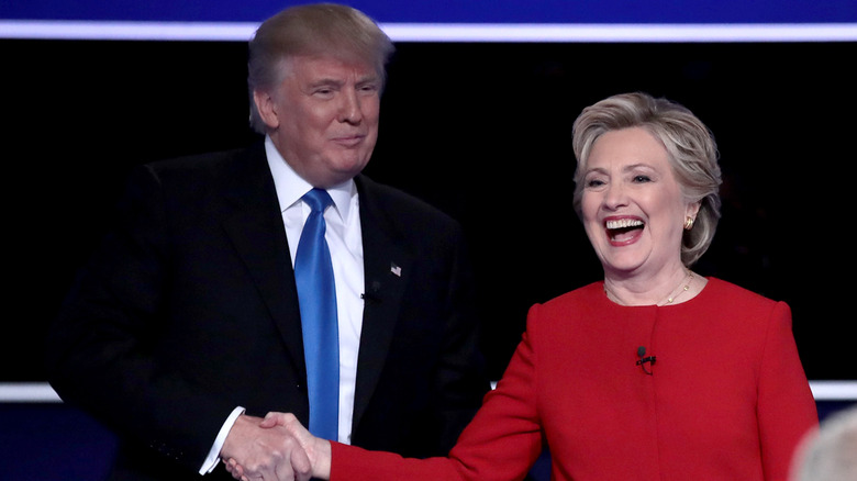 Hillary Clinton laughing while shaking hands with Donald Trump