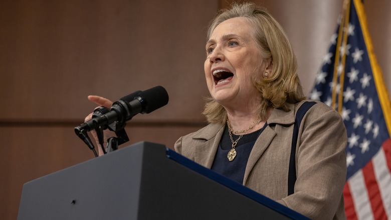 Hillary Clinton delivering an impassioned speech in a beige blazer and dark shirt while pointing