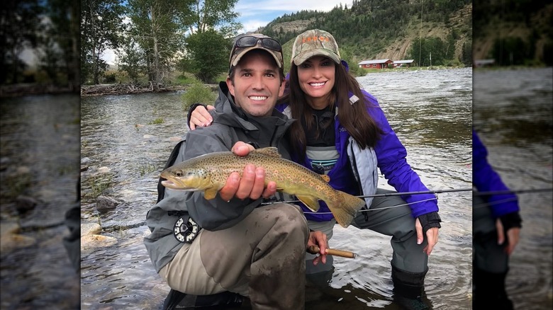 Kimberly Guilfoyle and Donald Trump Jr. pose for a photo with a fish while kneeling in a river