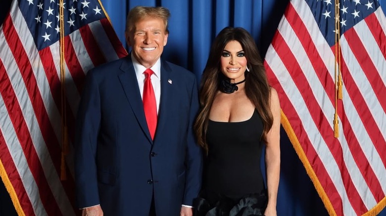 Kimberly Guilfoyle poses with President Donald Trump against a dark blue background and American flags