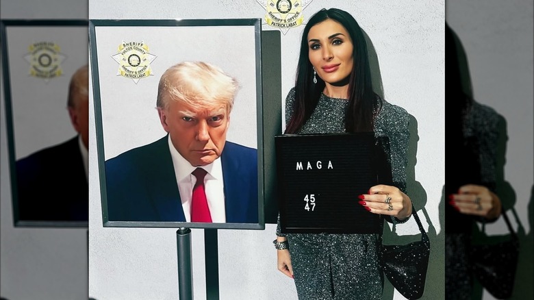 Laure Loomer stands with a printout of Donald Trump's mugshot while holding a sign that says "MAGA"