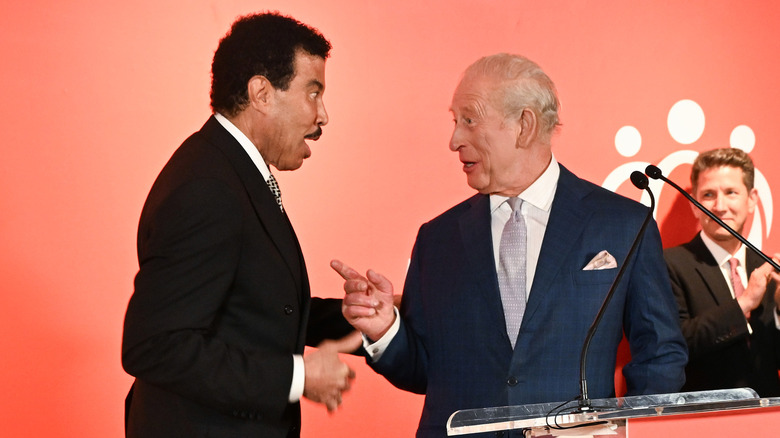 Lionel Ritchie looking surprised while King Charles talks and points