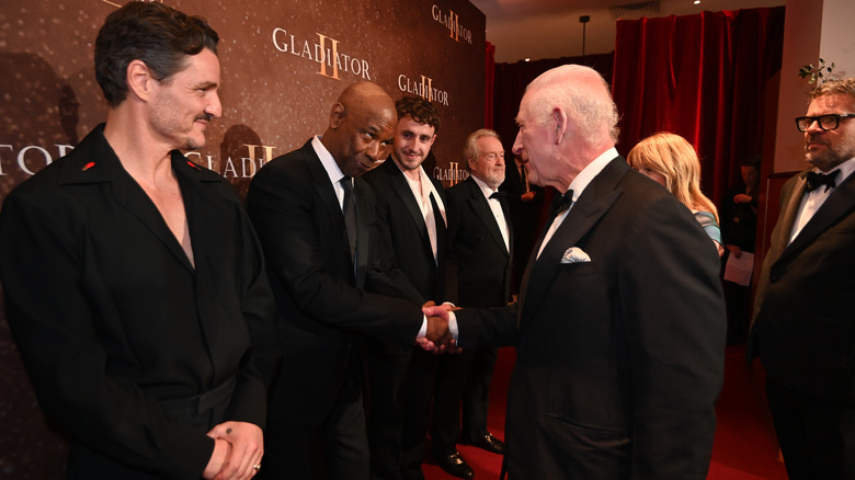Pedro Pascal smiling while Denzel Washington shakes hands with King Charles