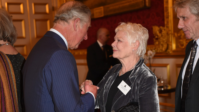 King Charles and Judi Dench holding hands and making strong eye contact