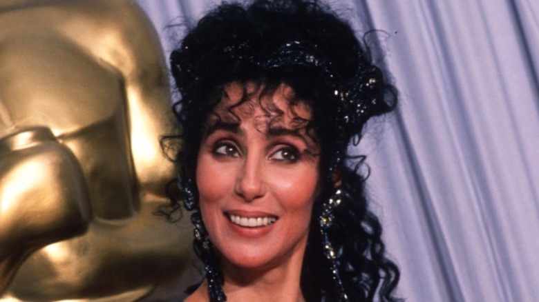 Closeup of Cher smiling in front of large Oscars statue