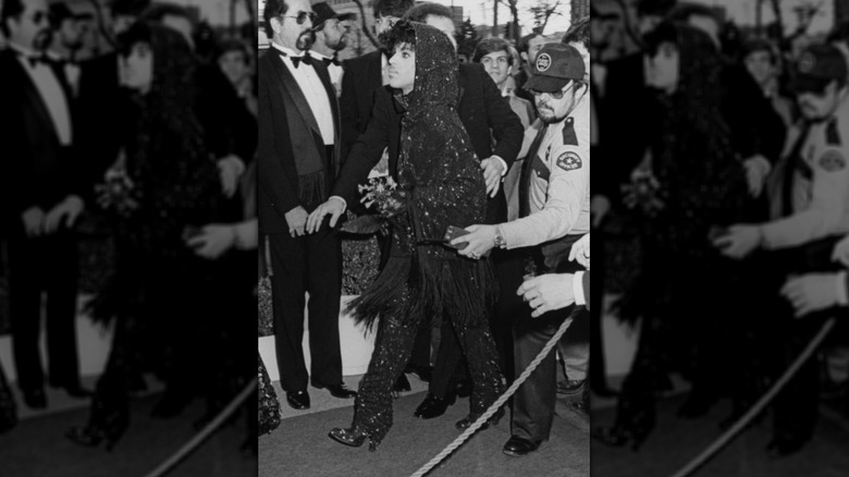 Prince in a sequined cape with a hood walking into event