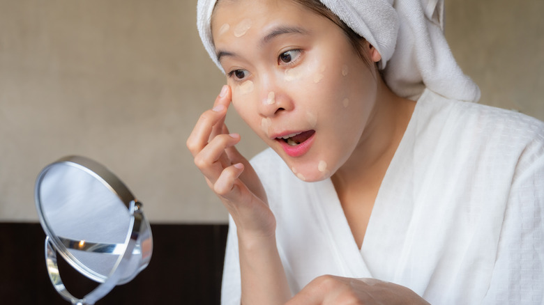 woman applying concealer in small mirror