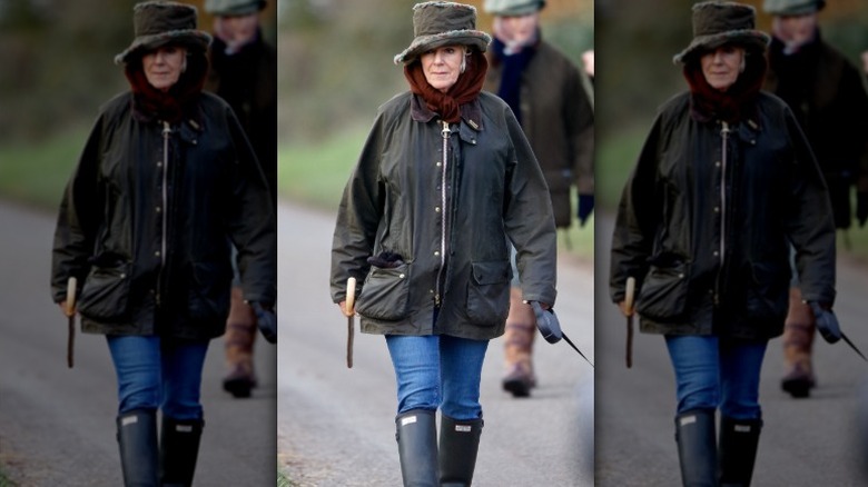Camilla, Queen Consort, walking outside in rain coat, jeans, and Hunter boots