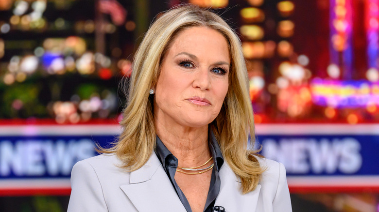 Martha MacCallum in a suit at a news desk with city lights behind her.