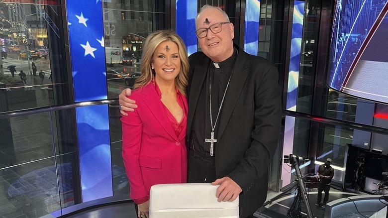 Martha Maccallum with an ash cross on her forehead, arm around a priest with a similar marking.