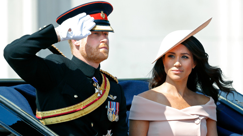 Prince Harry saluting and Meghan Markle looking serious