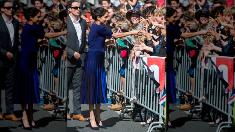 Meghan Markle in a blue skirt, smiling and greetings fans