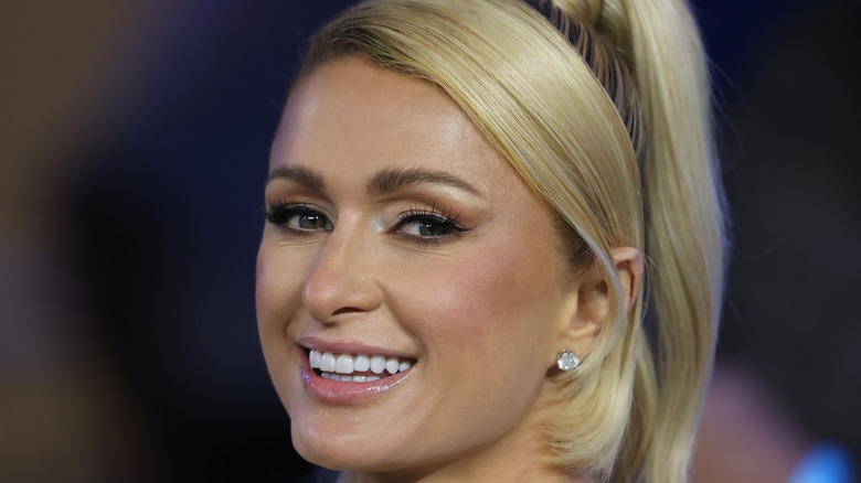 Paris Hilton smiling at the camera with a high ponytail