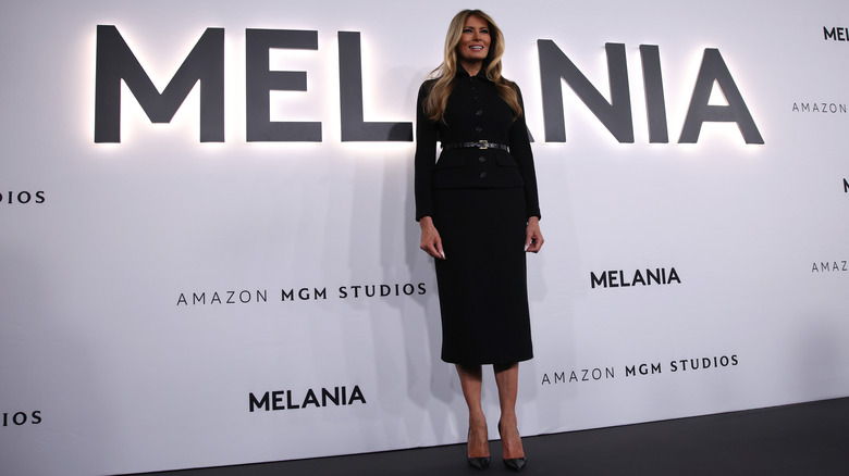 Melania Trump posing in front of a backdrop promoting her documentary