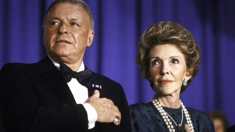 Frank Sinatra and Nancy Reagan with their hands over their hearts in front of a blue curtain