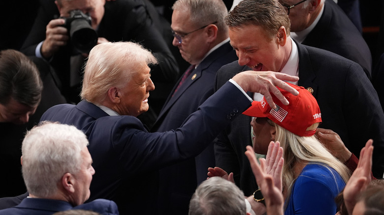 Donald Trump, among a crowd of congress men and women, with his hand on Marjorie Taylor Greene's head.