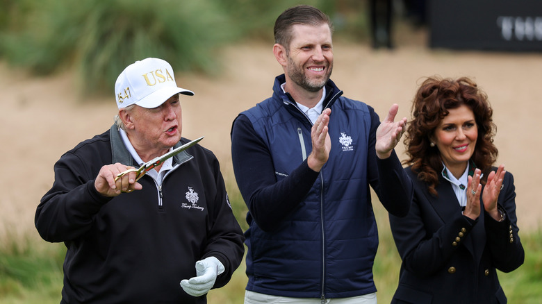 Donald Trump leaning toward holden scissors next to son on golf course.