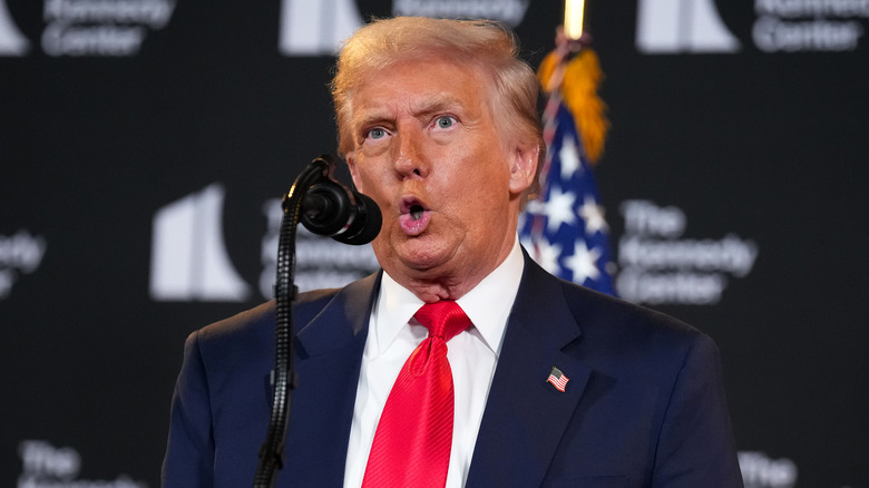 Donald Trump with wide eyes and his mouth open behind a mircophone.