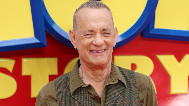 Tom Hanks smiling in front of 'Toy Story' logo