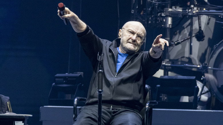 Phil Collins holding out the microphone to the crowd while performing on stage