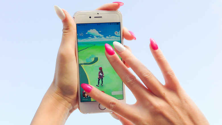 Woman holding a phone with an augmented reality game with pink and white painted fingernails