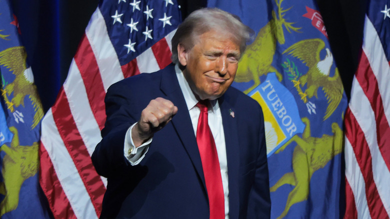 Donald Trump gesturing onstage at an event in a dark blue suit with a red tie