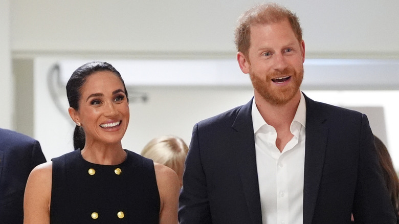 Meghan Markle in black sleeveless dress and Prince Harry smiling