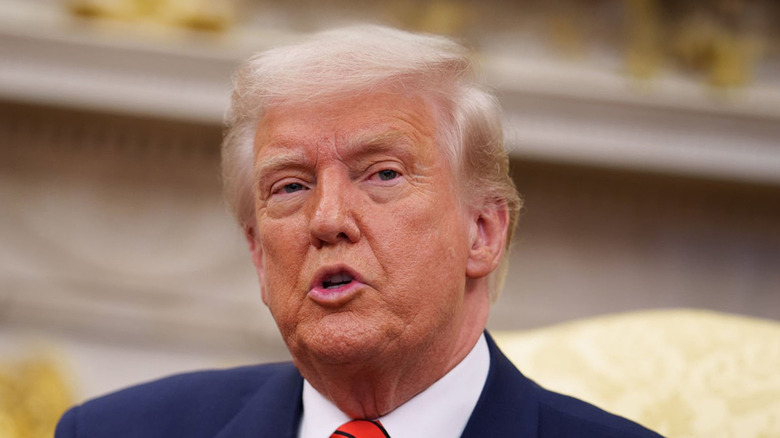Donald Trump sitting down speaking at the oval office while wearing a blue blazer, white collared shirt and red tie