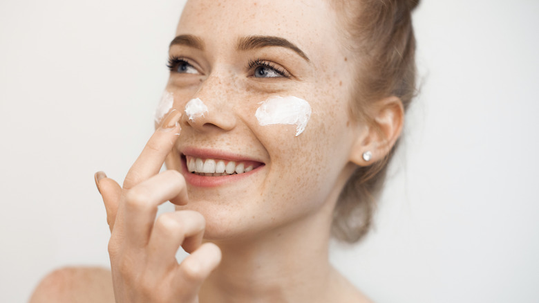 Woman smiling while applying face cream