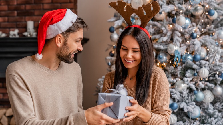 A couple exchanging gifts wearing Christmas themed clothes with a Christmas tree in the background