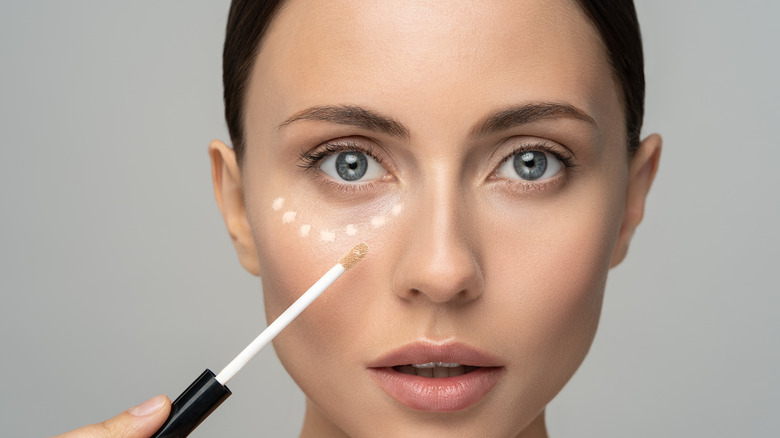 A woman applying dots of concealer under her eyes 