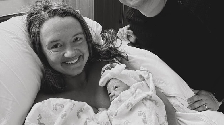 Alex Drummond smiling in hospital bed holding baby